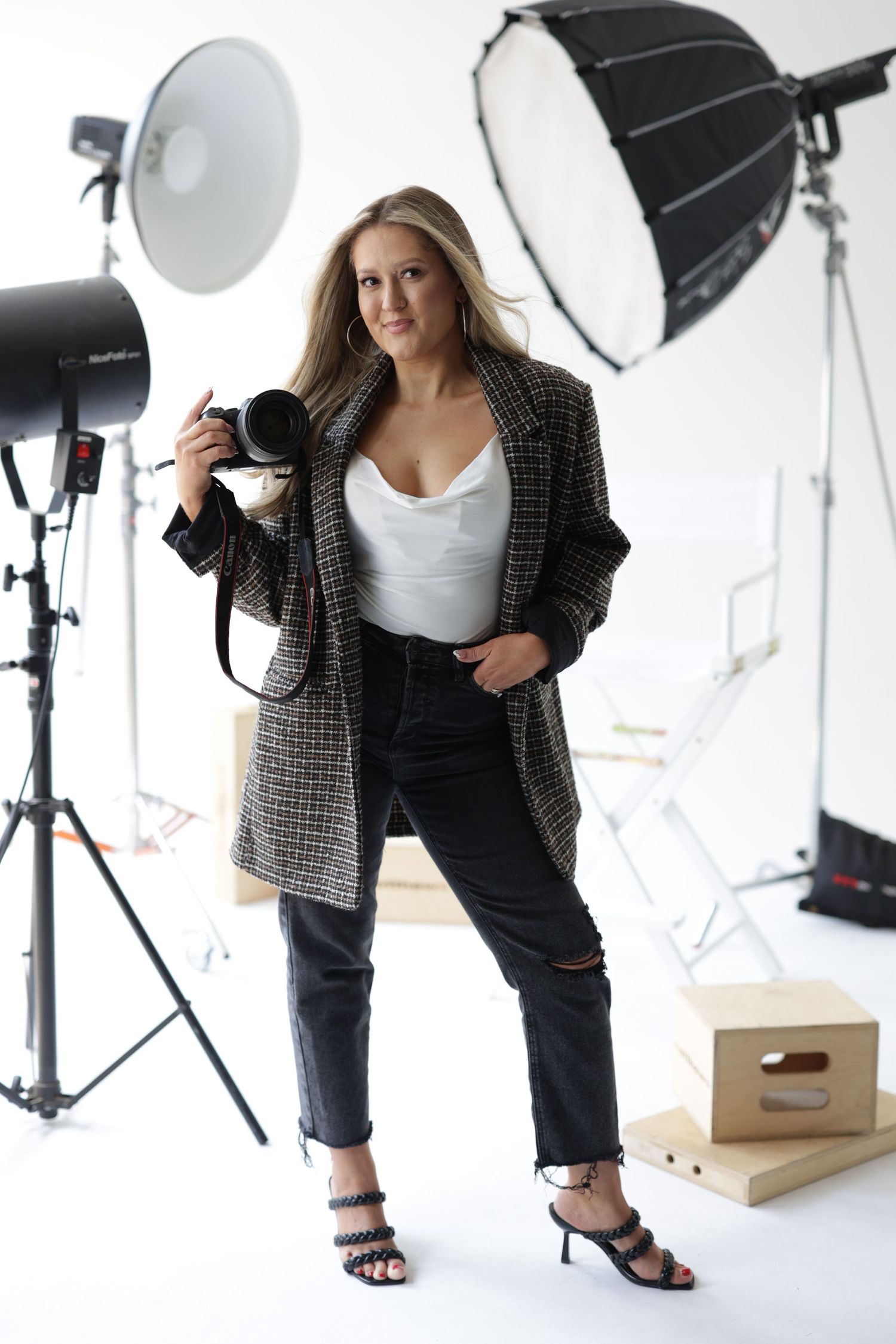 Female photographer holding camera in professional studio with lighting equipment and softboxes.