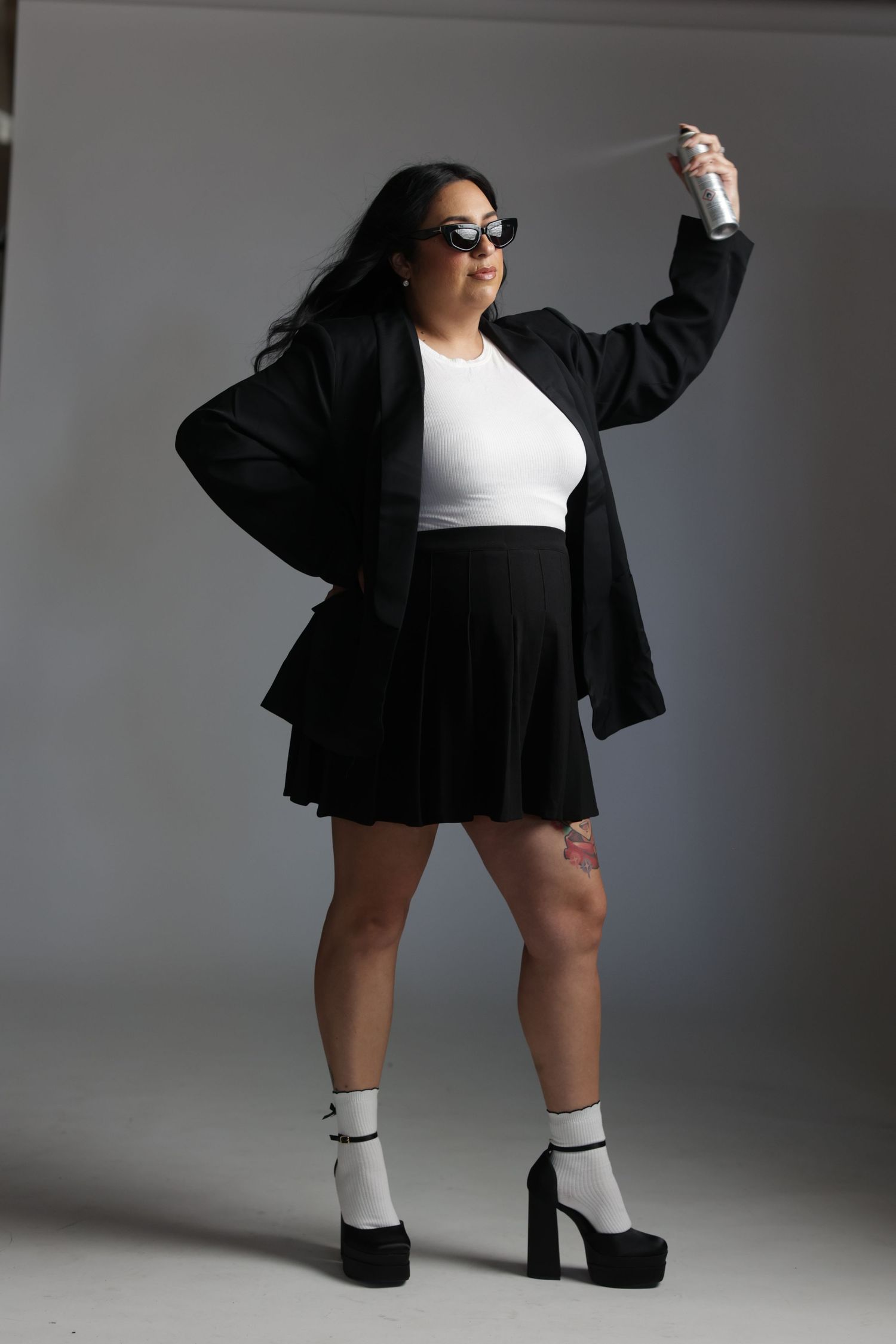 Woman in black skirt white top and sunglasses holding spray can in photo studio.