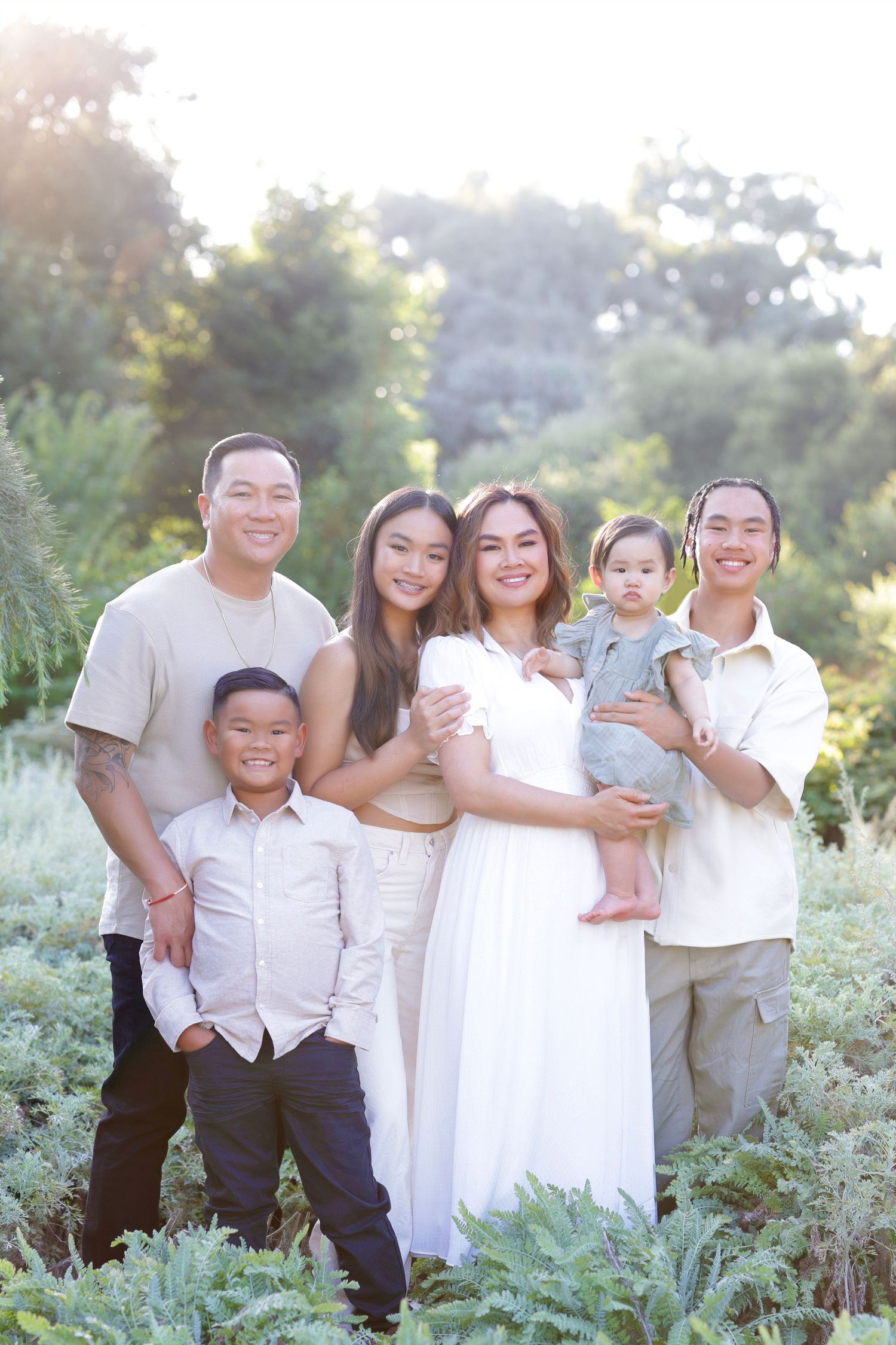 Happy Asian family of six posing together in sunlit green outdoor field during golden hour.