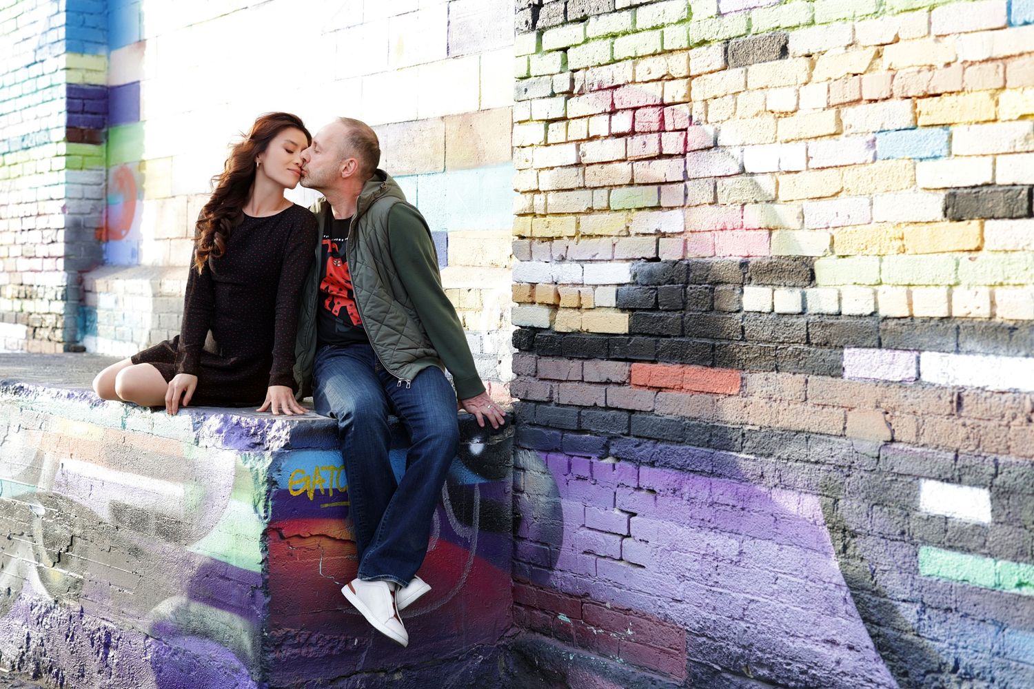 Couple sharing a romantic moment on a colorful graffiti-covered brick wall outdoors.