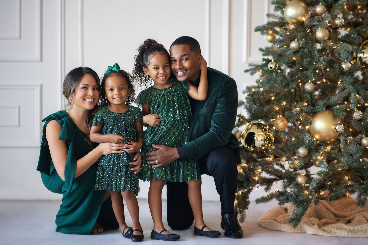 Family of four in matching green outfits posing together beside a decorated Christmas tree.