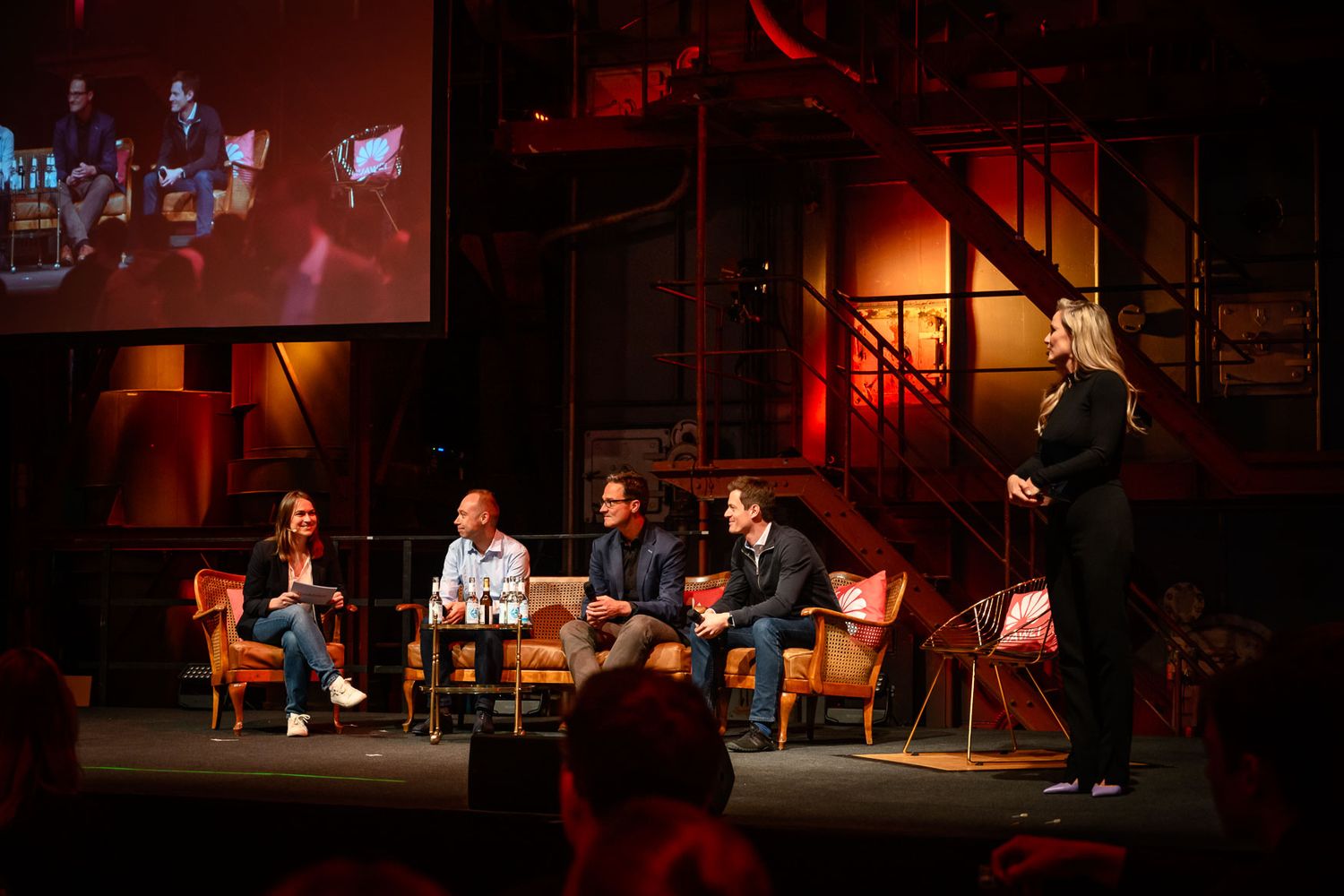 Panel discussion taking place on dimly lit stage with projection screen in background.