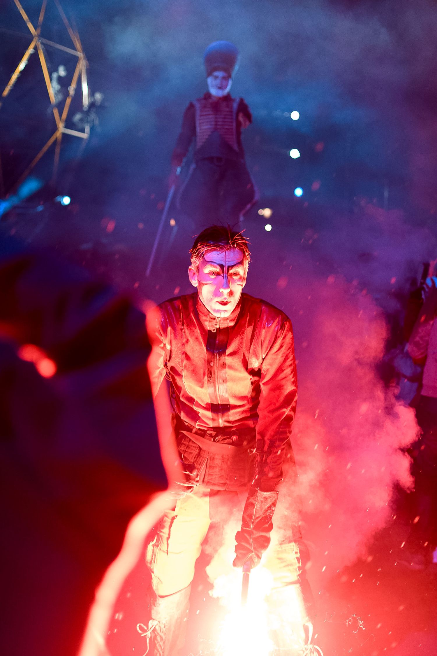 Theatrical performance with performers in dramatic red lighting and smoke effects on stage.
