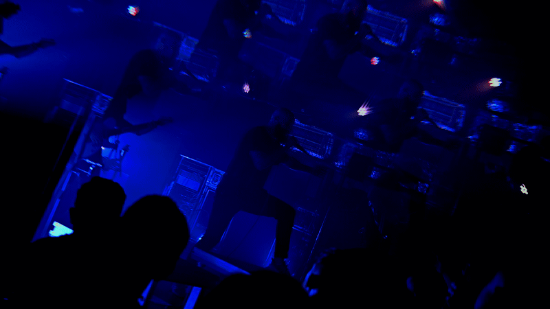 Dark nightclub interior lit with blue lights and silhouettes of audience members.