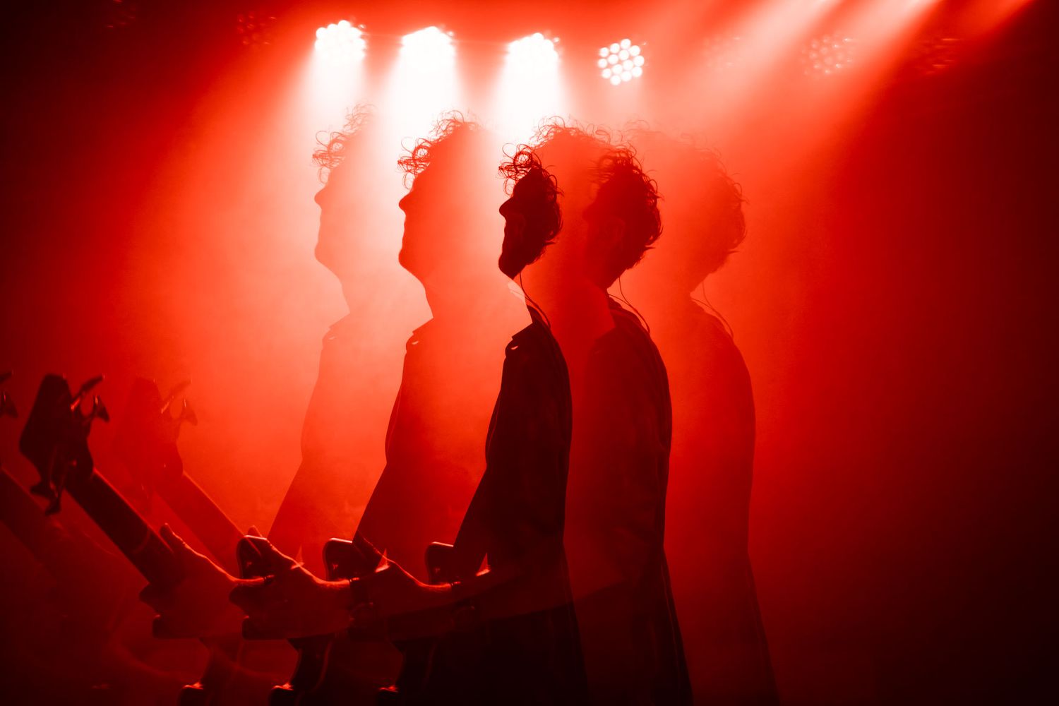 Silhouetted figure in dramatic red lighting creating multiple ghost-like reflections during stage performance.