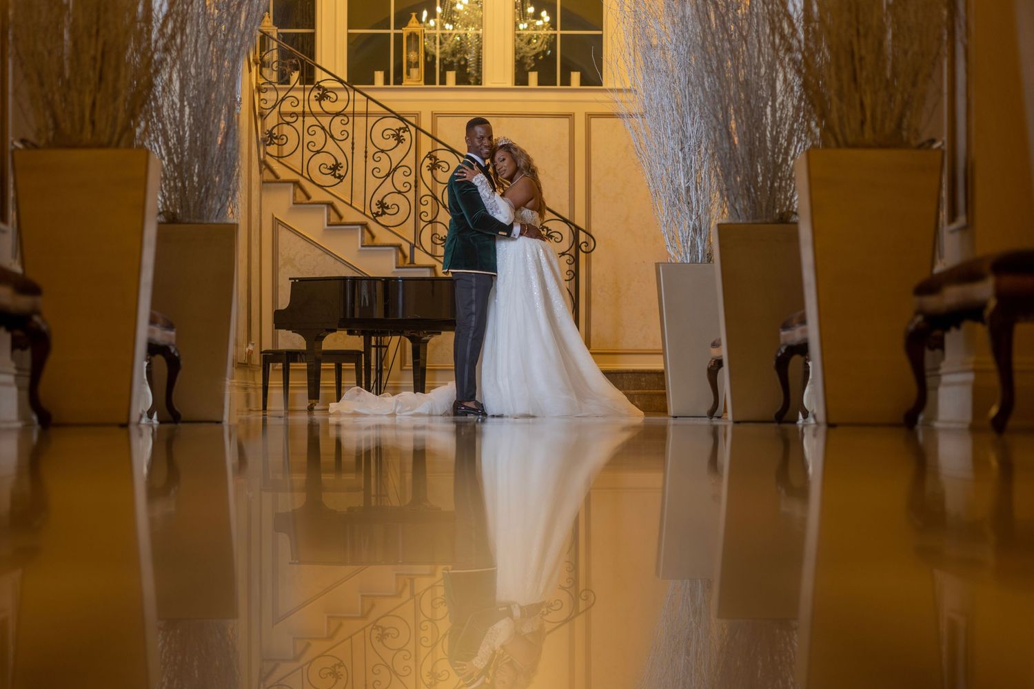 Elegant wedding couple sharing a romantic kiss in a grand ballroom with golden staircase and sparkling trees.