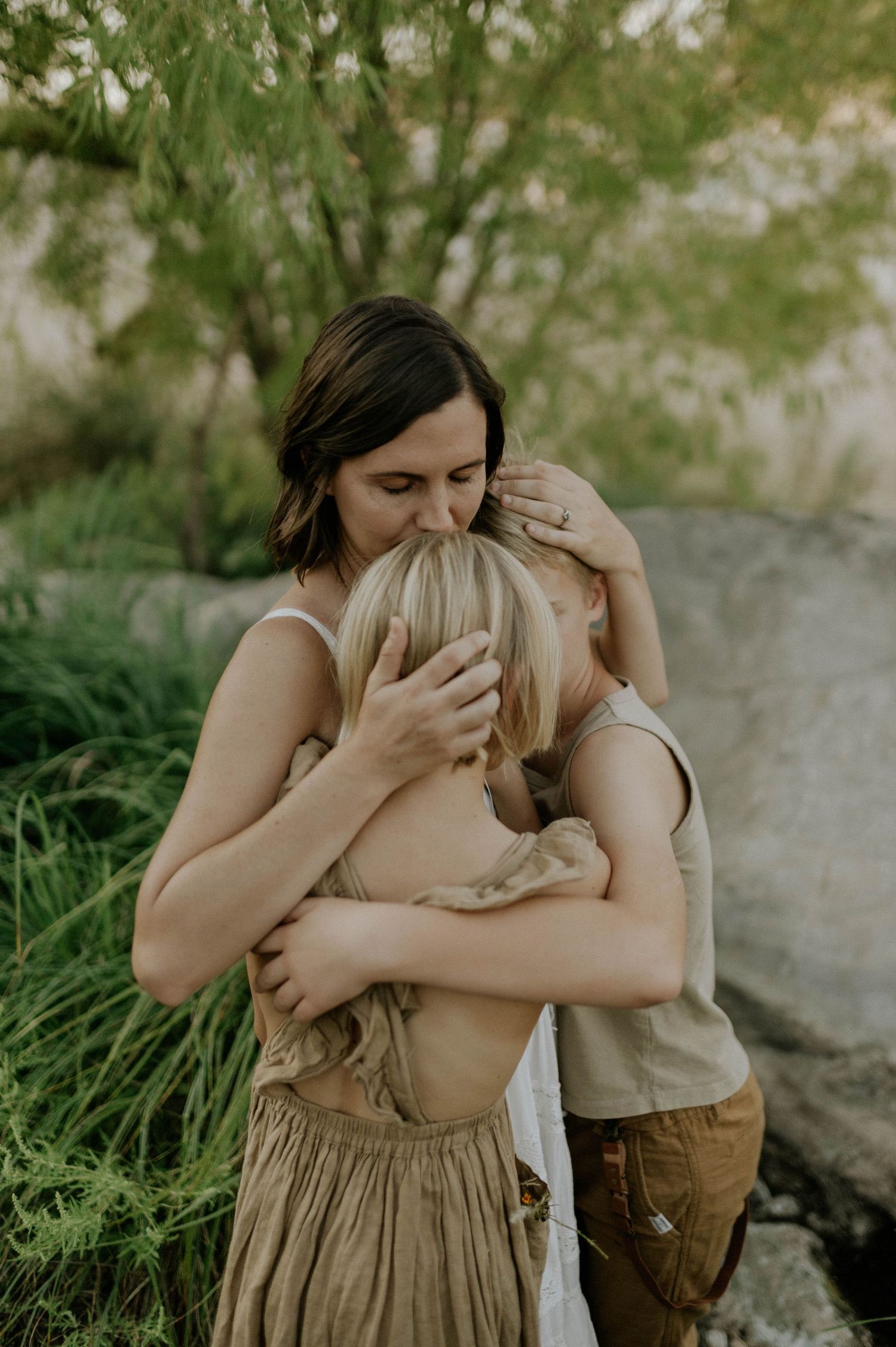 Emotional group hug between mother and two children surrounded by lush green nature outdoors.