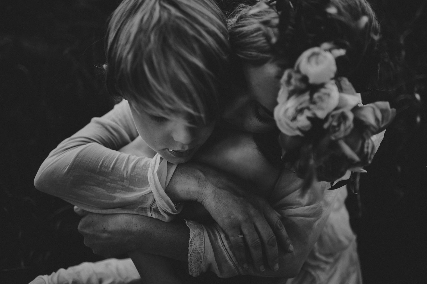 Intimate black and white close-up of a child embracing an adult wearing a floral crown.