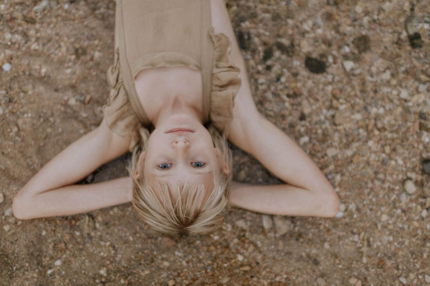 Overhead view of a blonde child lying peacefully on sandy ground.