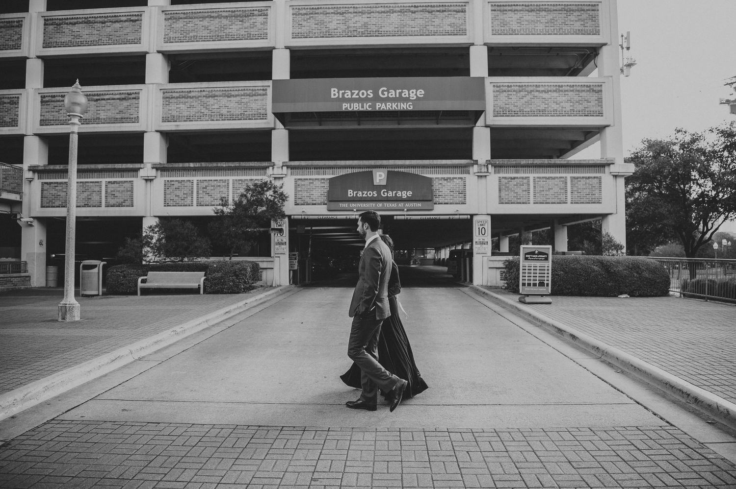 Black and white photo of woman in long dress walking past urban parking garage.