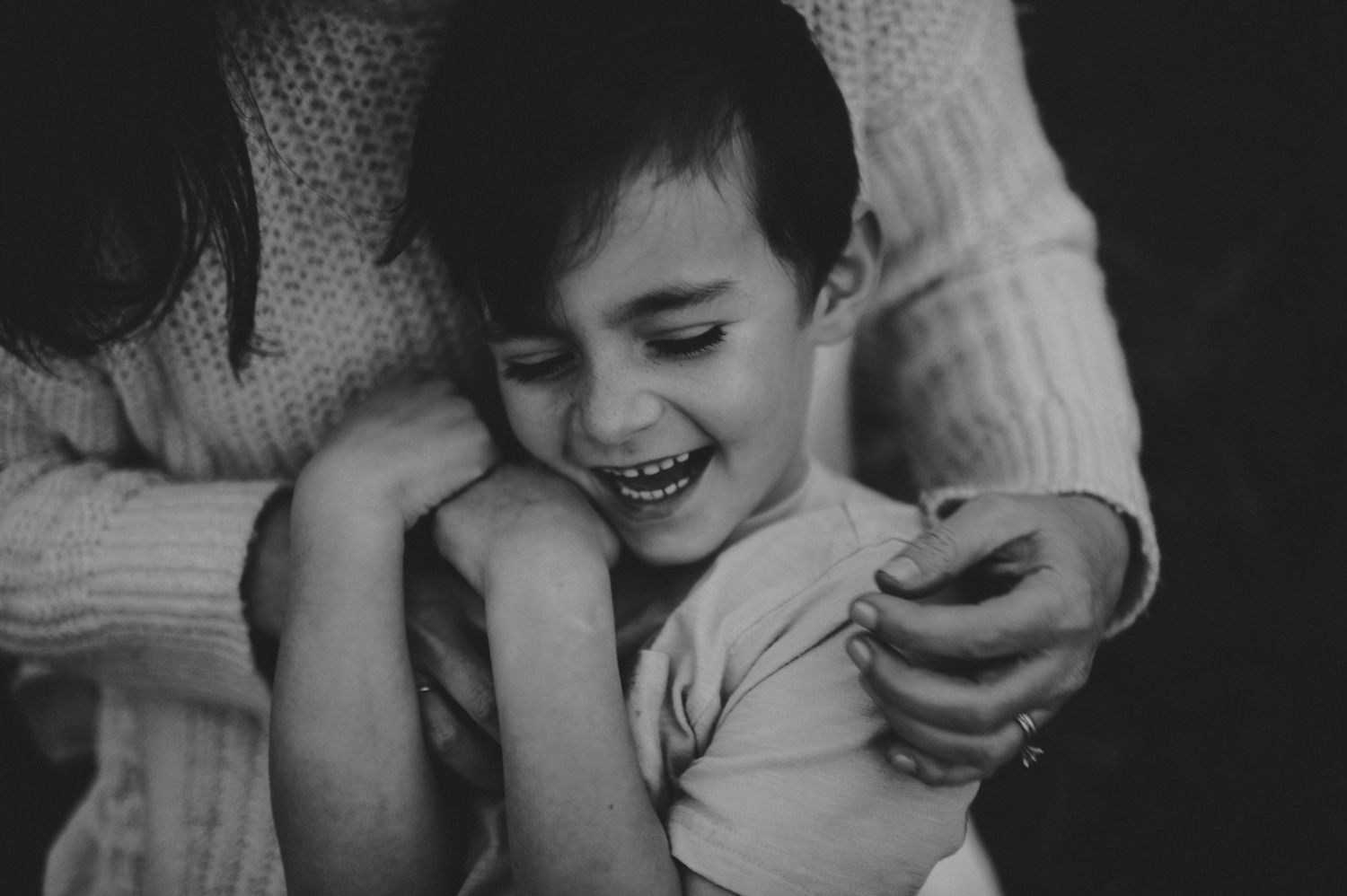 Black and white photo of a laughing child being hugged by an adult in a cozy knit sweater.