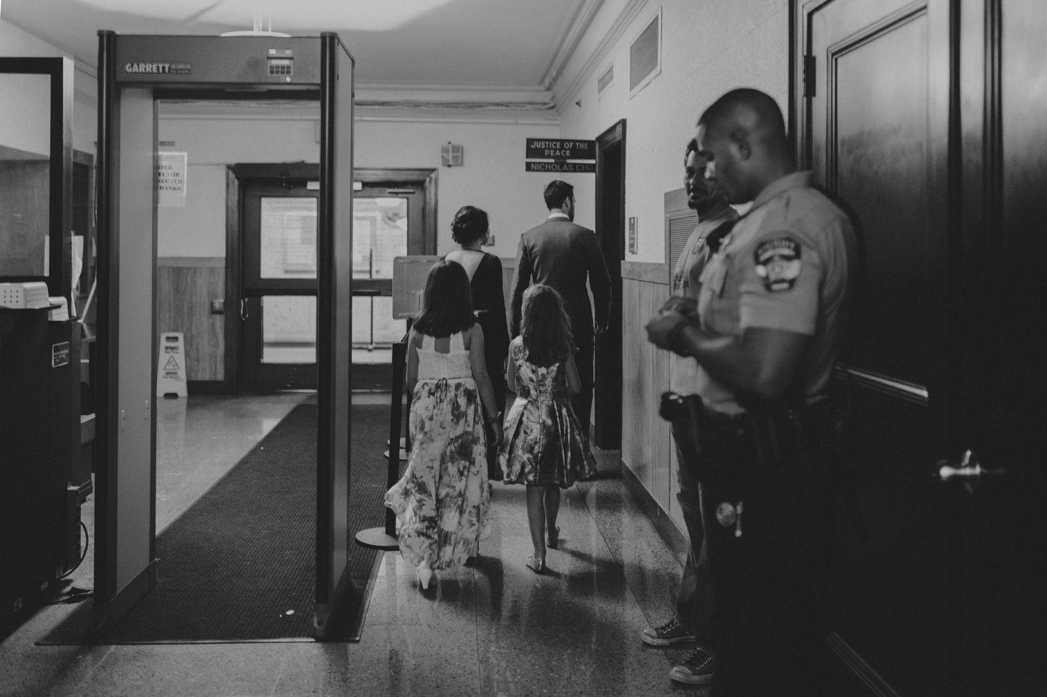 Security officer stands by a metal detector as guests enter a building.