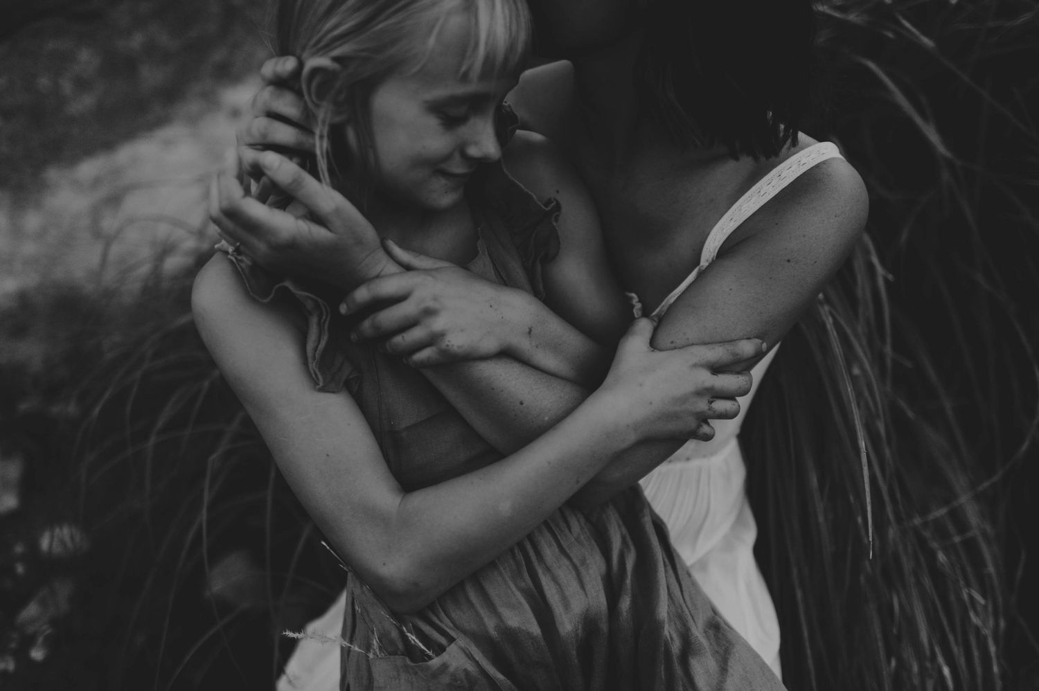Black and white photo of two women sharing a close intimate embrace outdoors in nature.