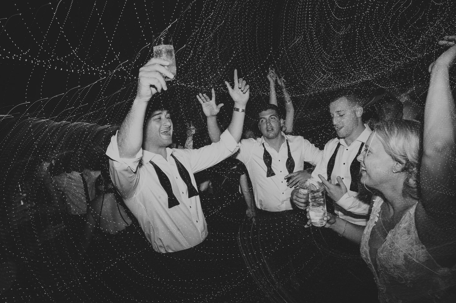 Groomsmen celebrating on the dance floor at a wedding reception in black and white.