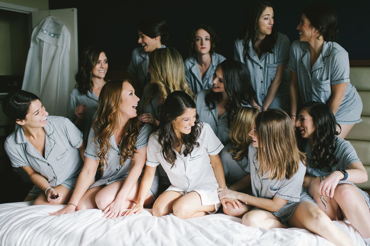 Bridesmaids in matching gray pajamas laughing together on a bed before the wedding.