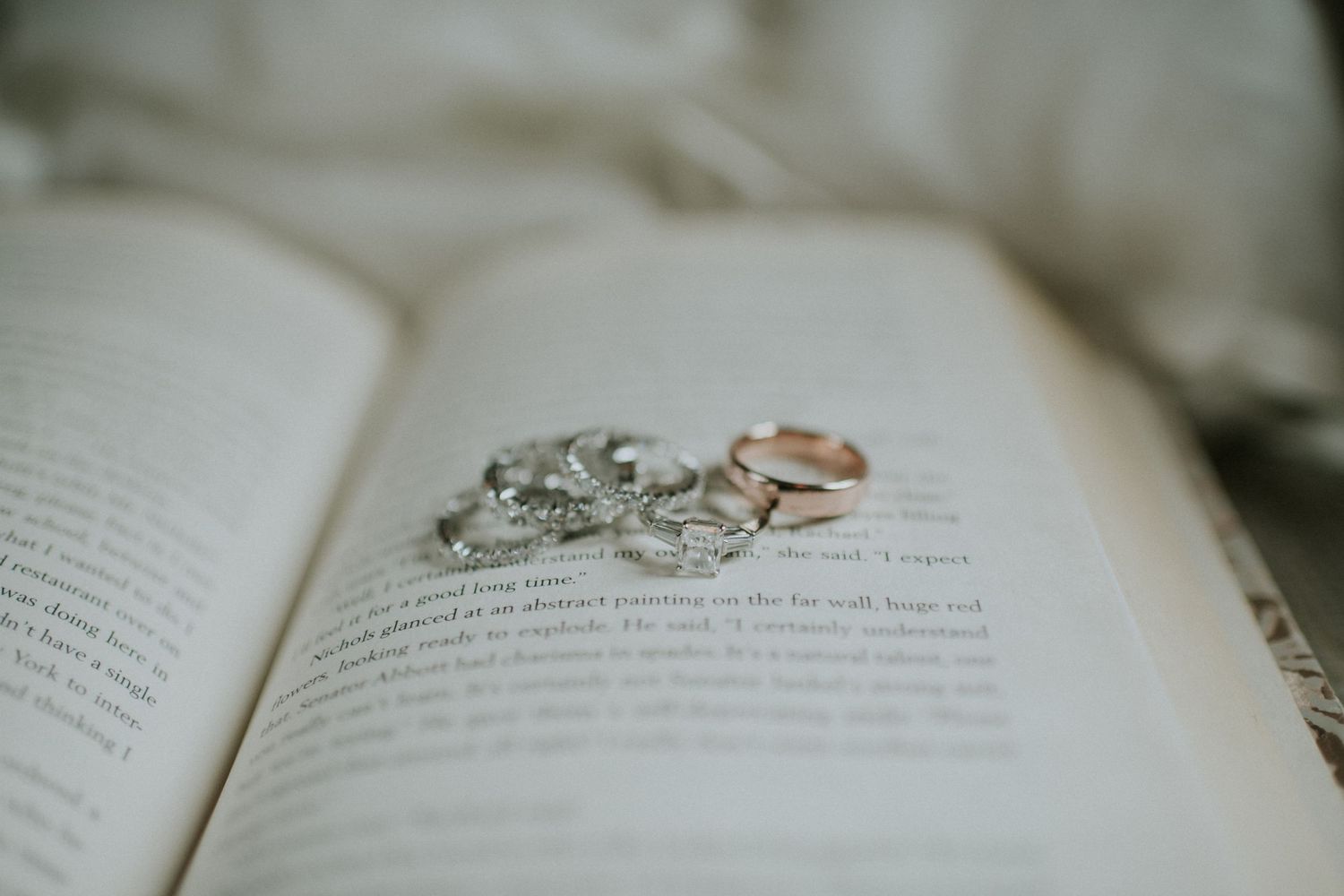 Wedding rings and a sparkling diamond bracelet resting on the pages of an open book.