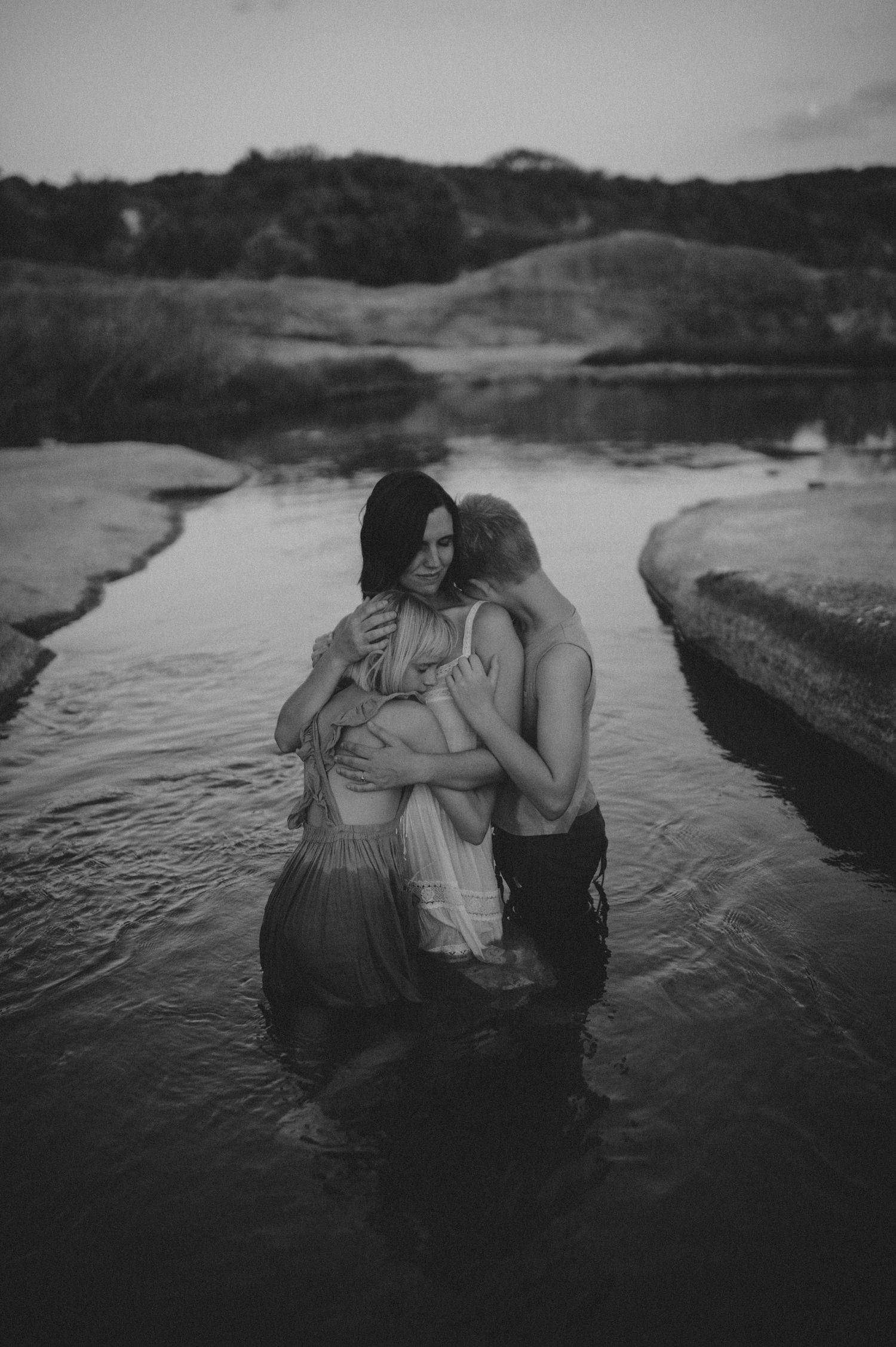 Black and white image of a family sharing a warm embrace while standing in a river.