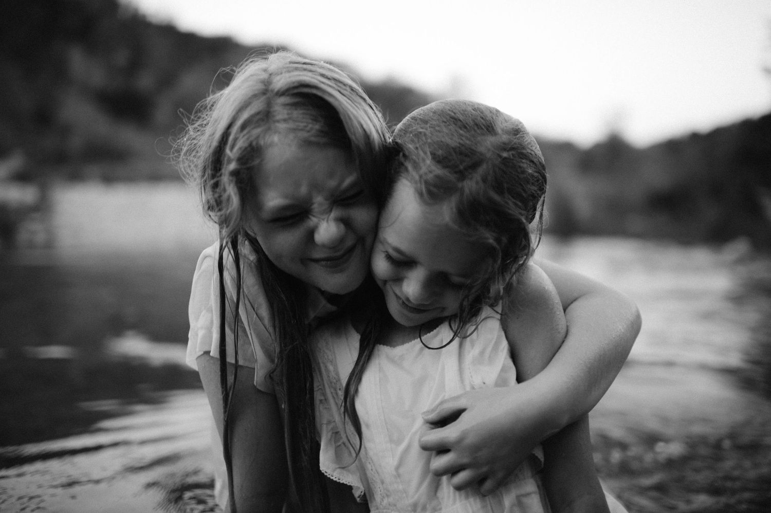 Black and white photo of a woman and young girl hugging and smiling near a river.
