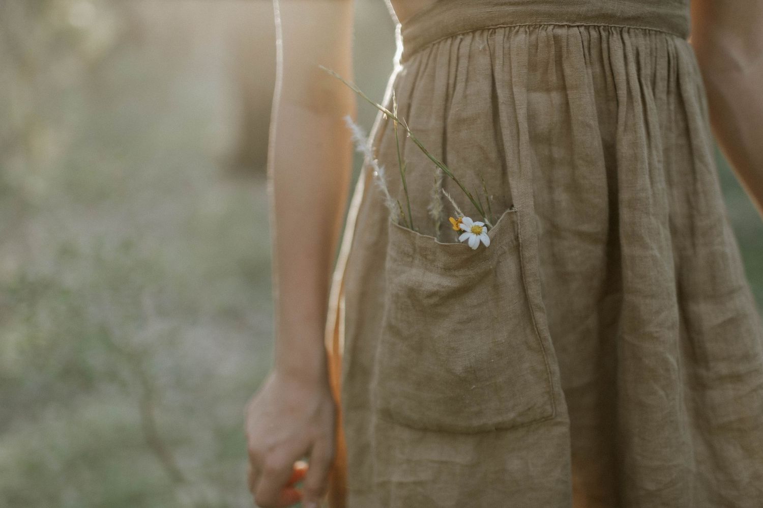 Close-up of a woman in an olive linen dress with small white flowers tucked into the pocket.