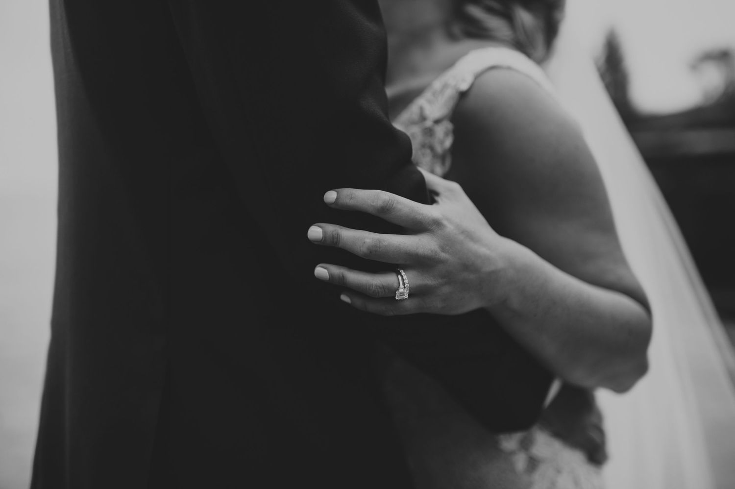Black and white close-up of bride embracing groom, showcasing diamond engagement ring.