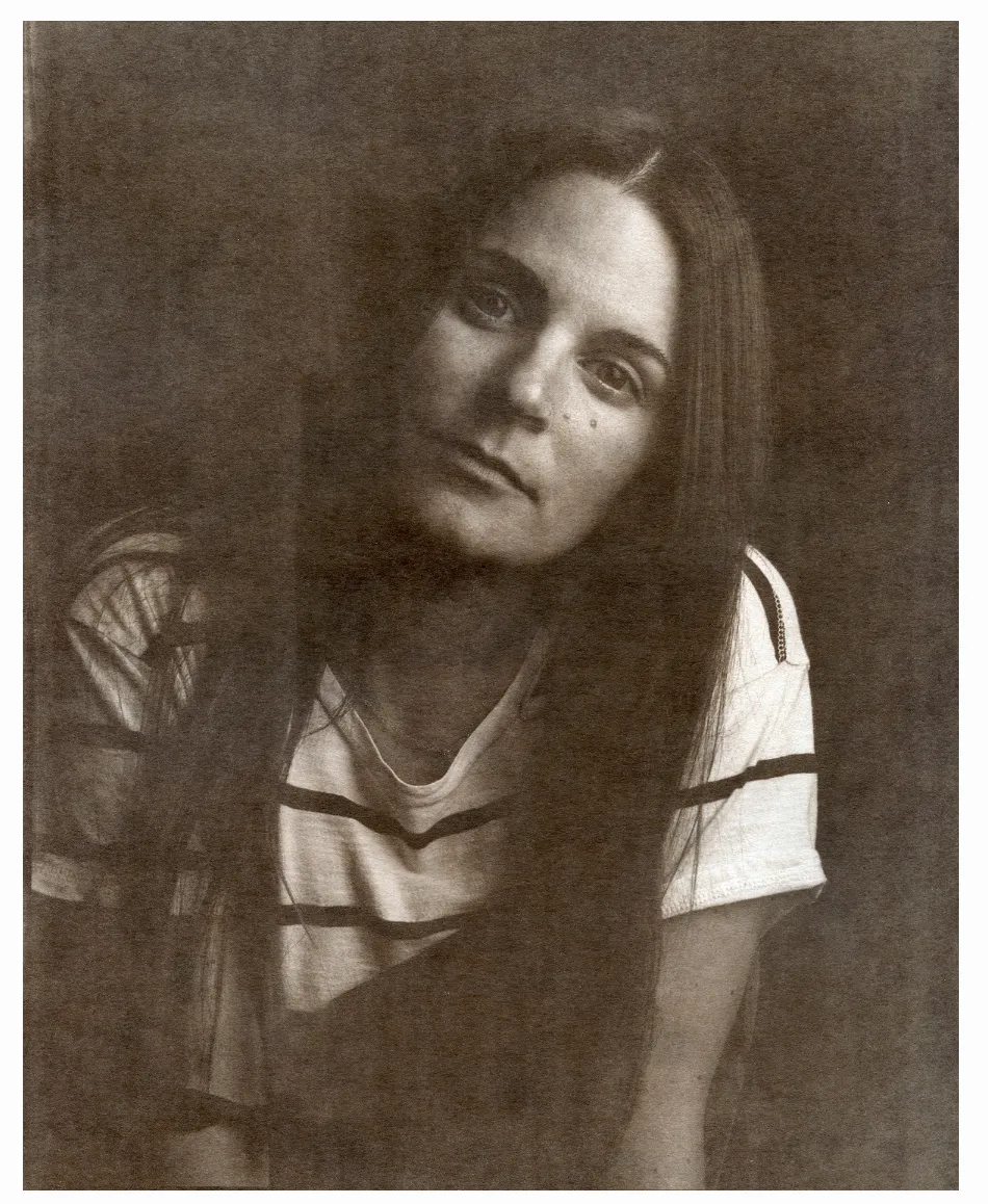 A vintage-style black and white portrait of a woman in a striped shirt with a contemplative gaze.