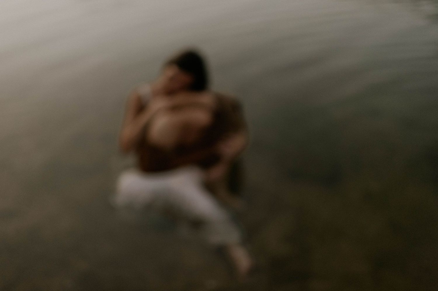 Couple embracing and lying in shallow water, captured in a dreamy blurred photography style.