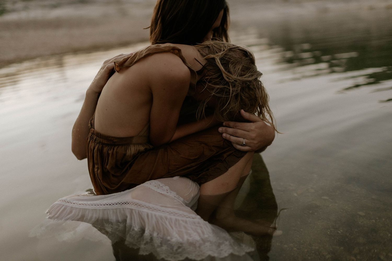 Two people sharing a warm embrace while sitting in shallow water.