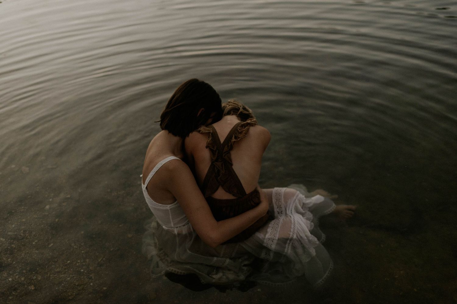 Woman in white dress embracing another person while sitting in calm water.