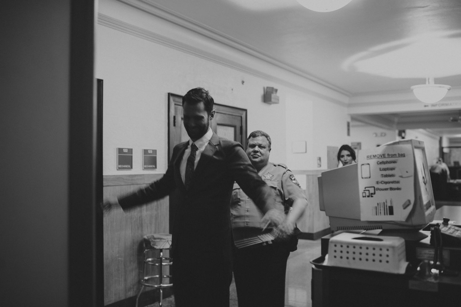 A man in a suit is patted down by a security officer in a building entrance.