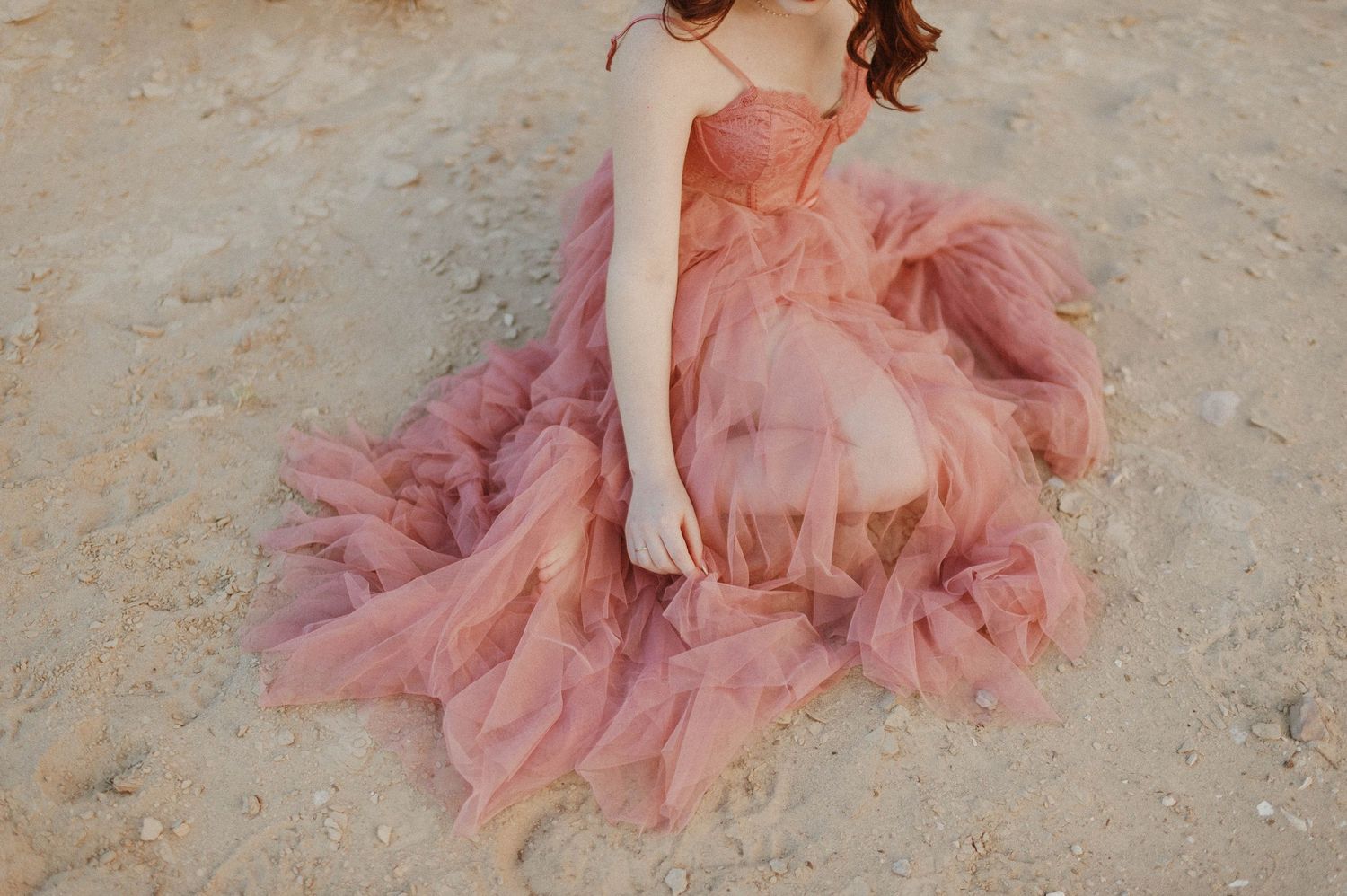 Overhead view of woman in layered blush pink tulle gown sitting on sandy desert ground.