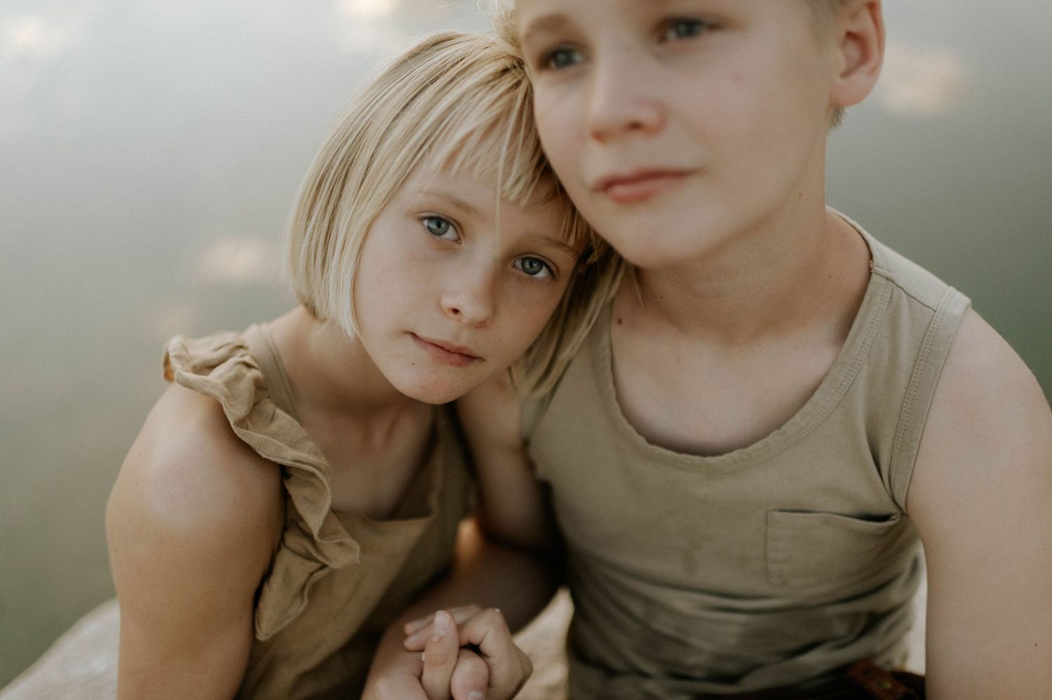 Two blonde children, a girl and boy, share a tender embrace while holding hands outdoors.