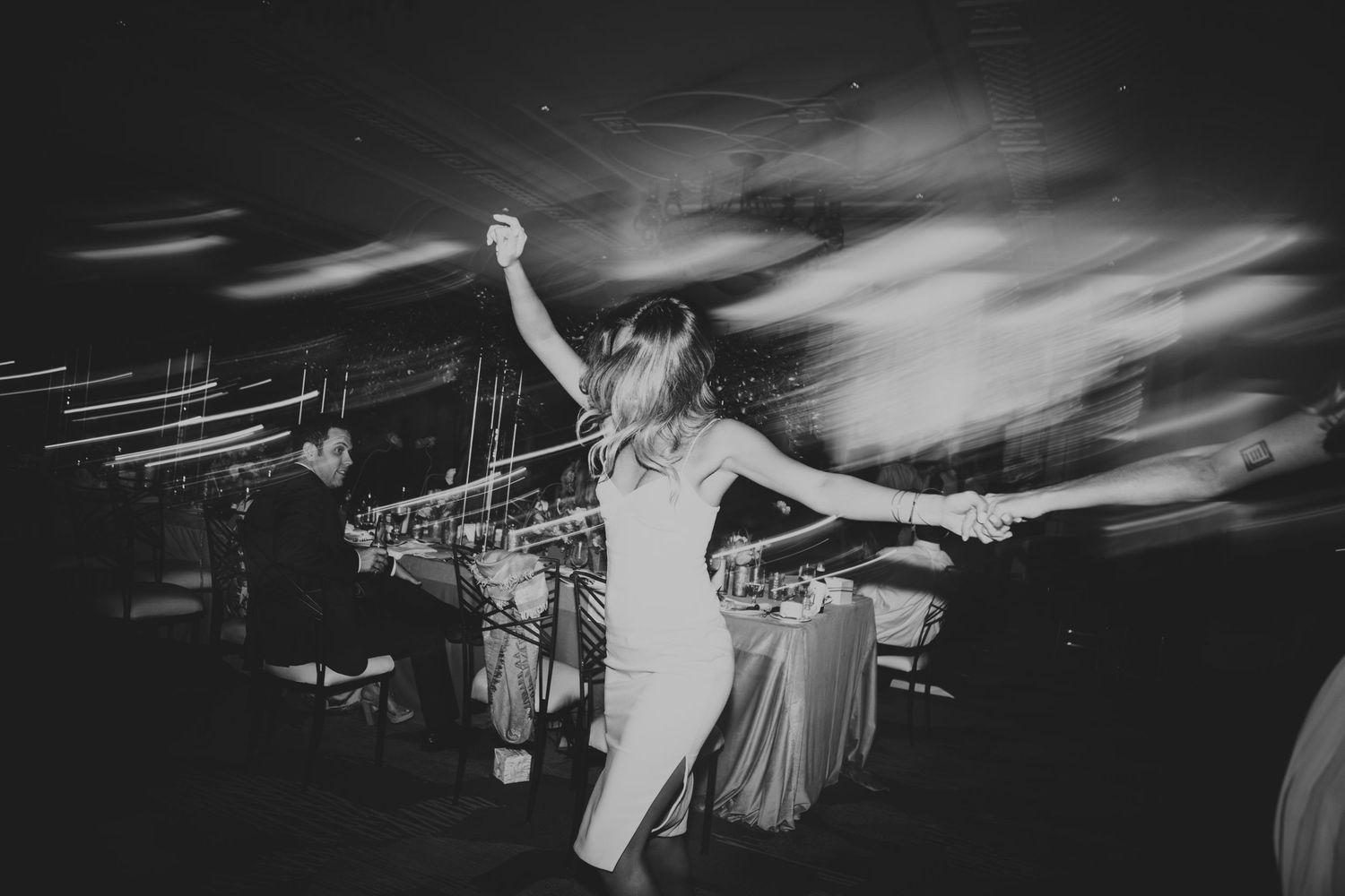 Black and white photo of a woman dancing at a wedding reception with a DJ performing in the background.