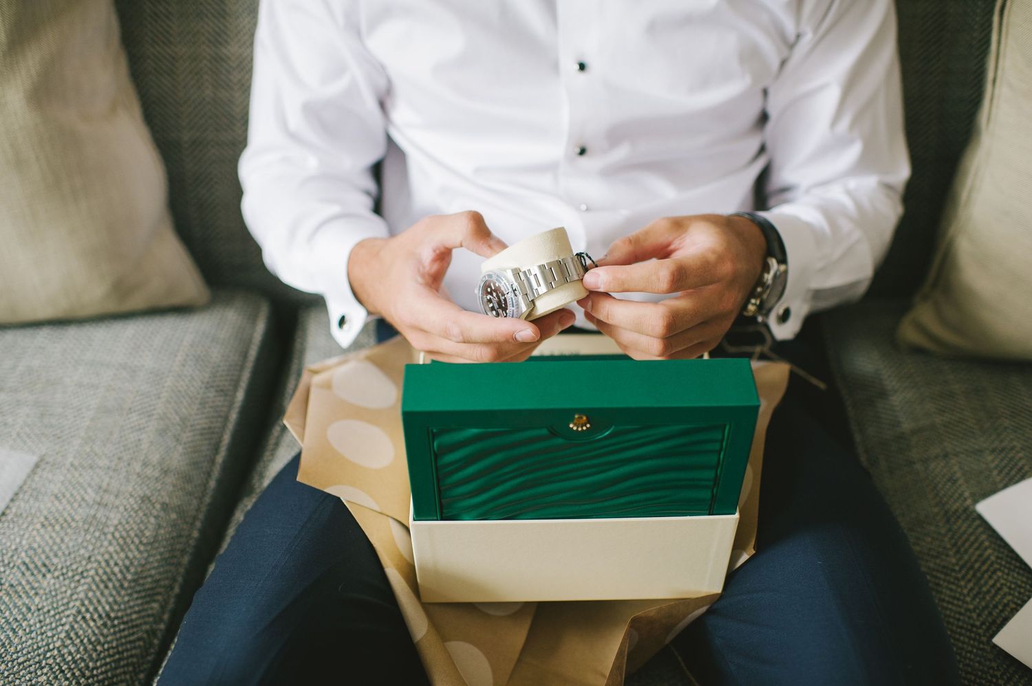 Groom opens a Rolex watch gift box while seated on a couch before wedding.