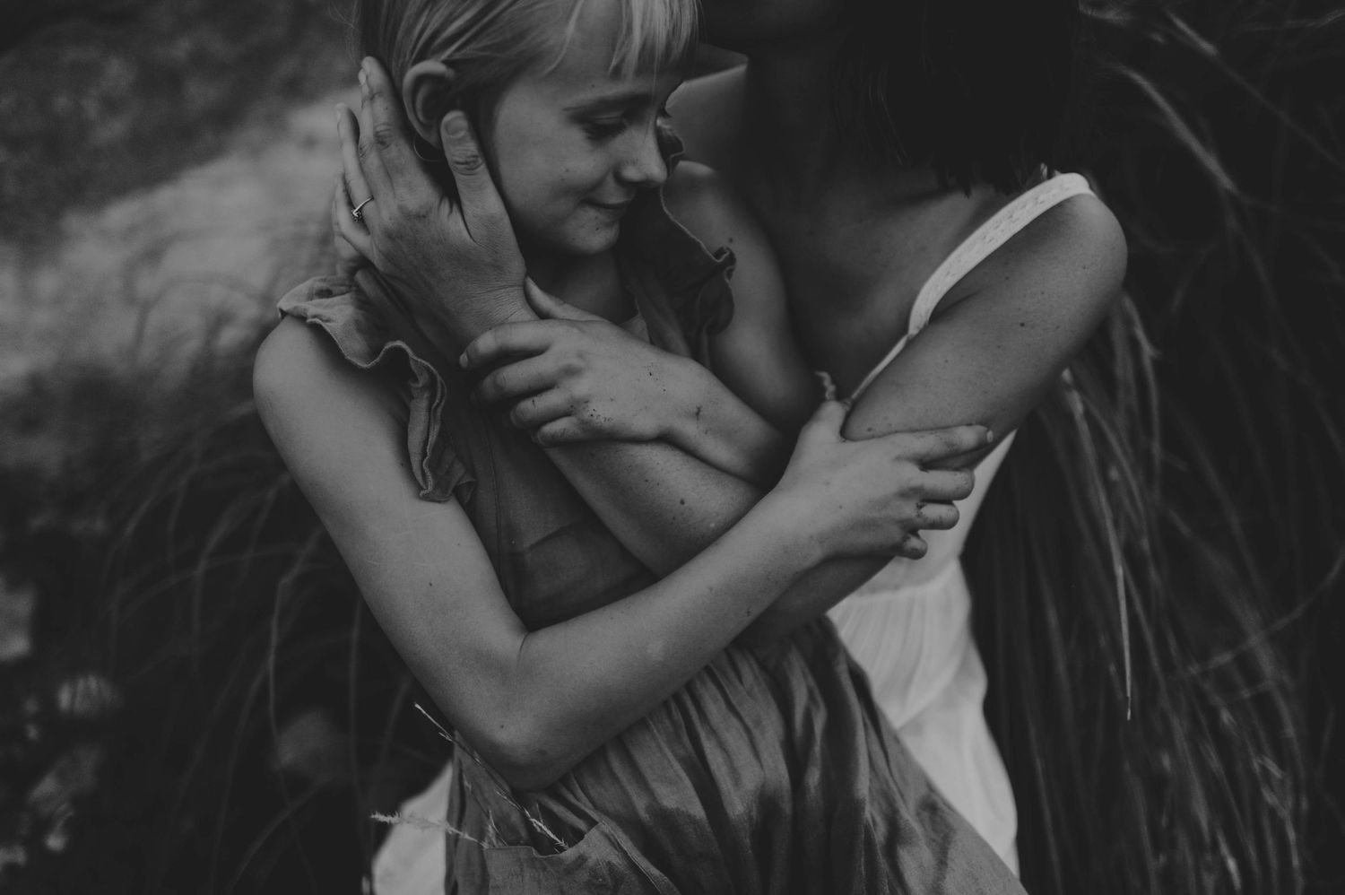 Black and white image of a smiling young girl being tenderly embraced by her mother.