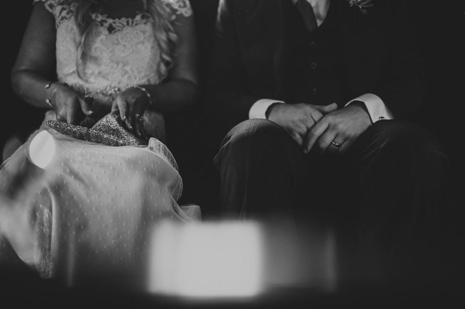 Black and white close-up of bride and groom sitting together during wedding ceremony.