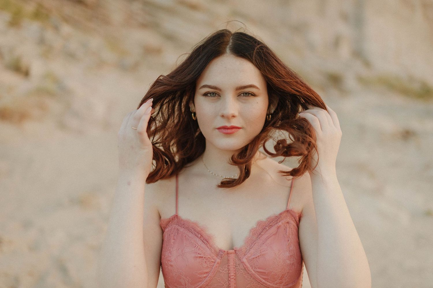 Young woman with dark hair wearing a pink lace bustier top poses outdoors in a desert setting.