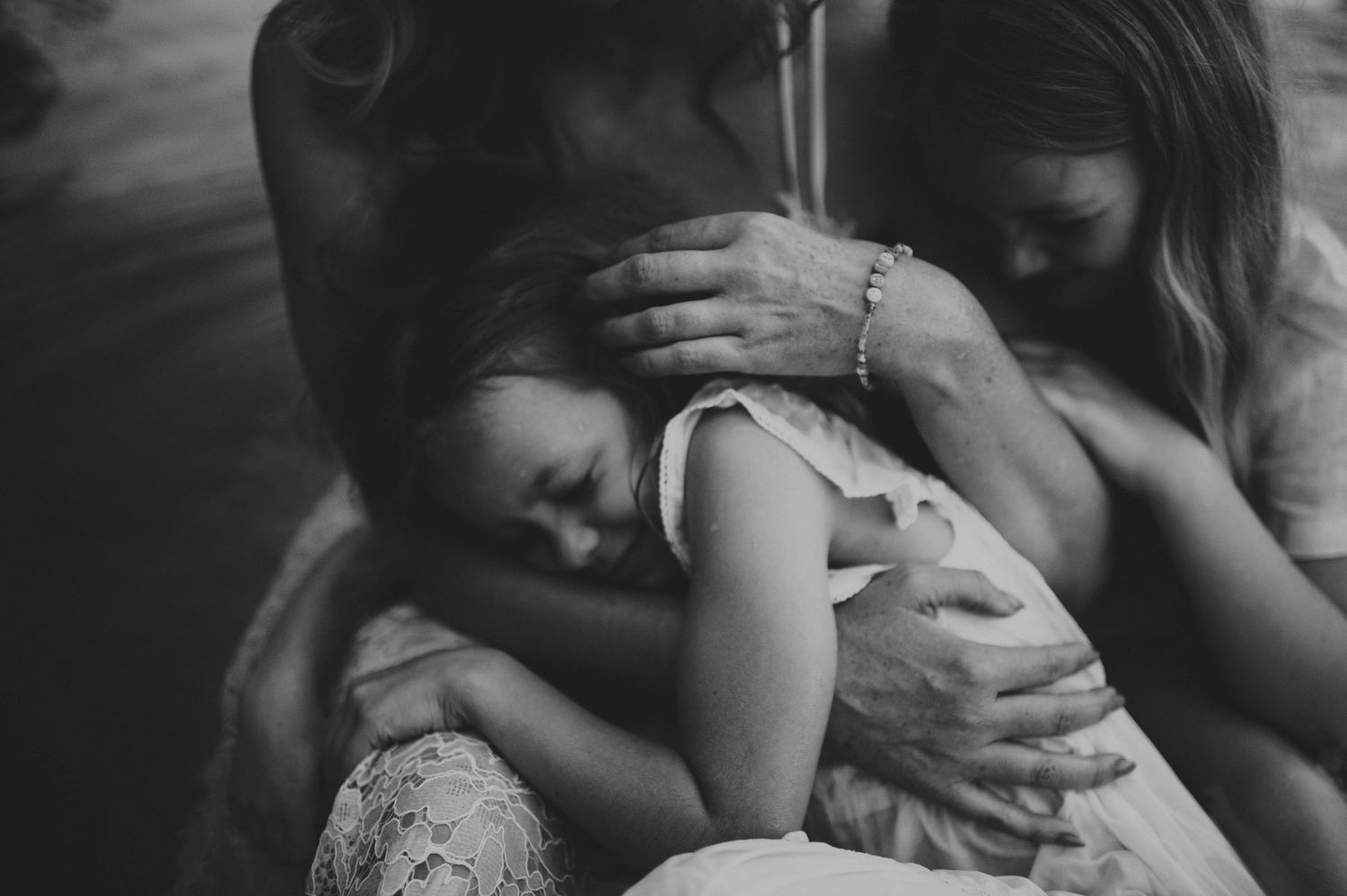 Black and white photo of parents tenderly embracing their young child in an intimate family moment.