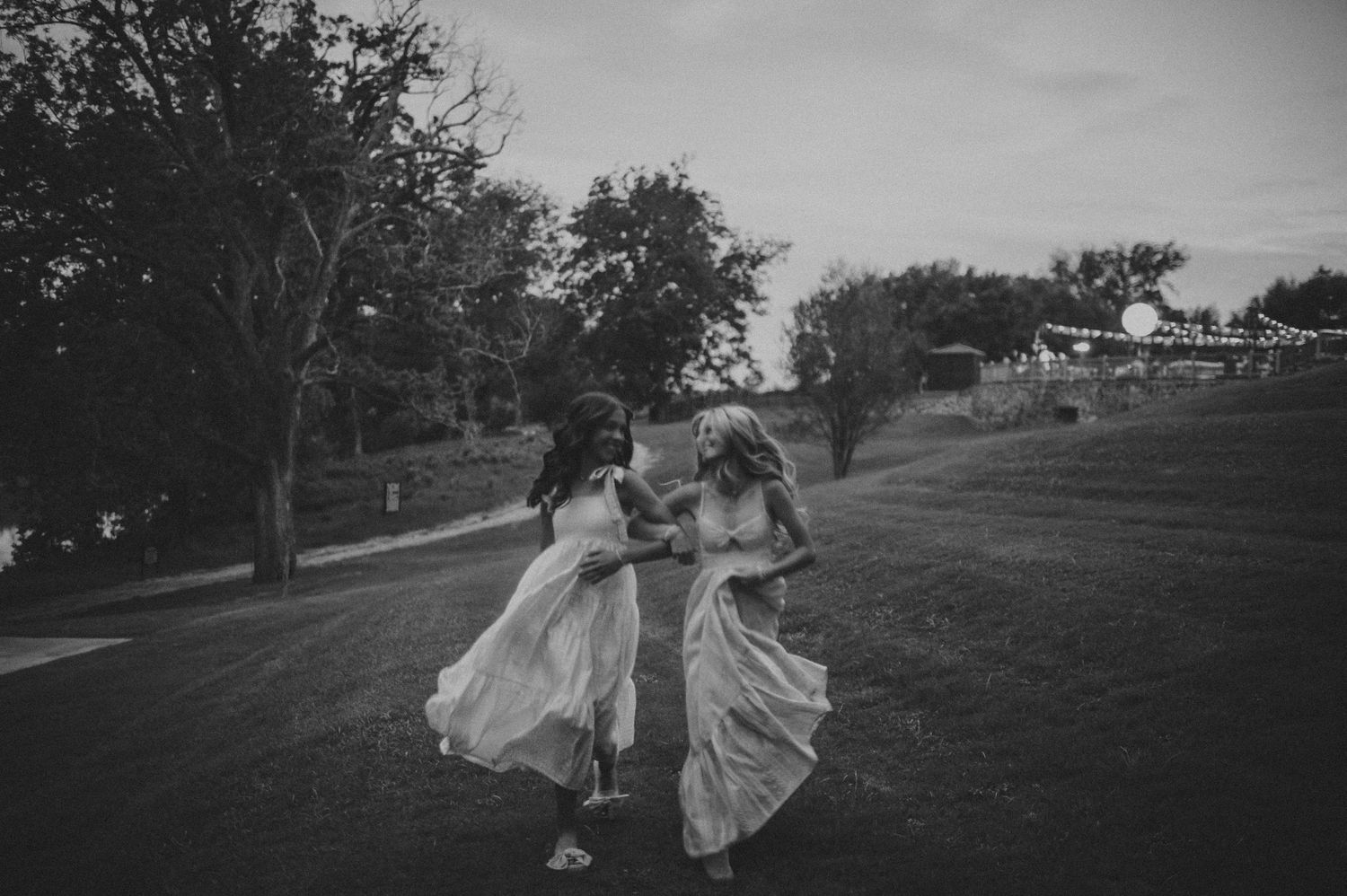 Black and white photo of two women in flowing dresses dancing joyfully on a grassy lawn.