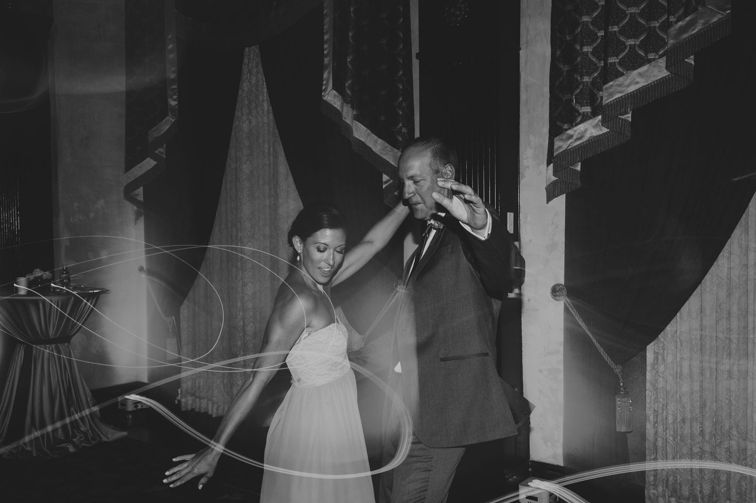 Black and white photo of bride and groom dancing at wedding reception with light trails.