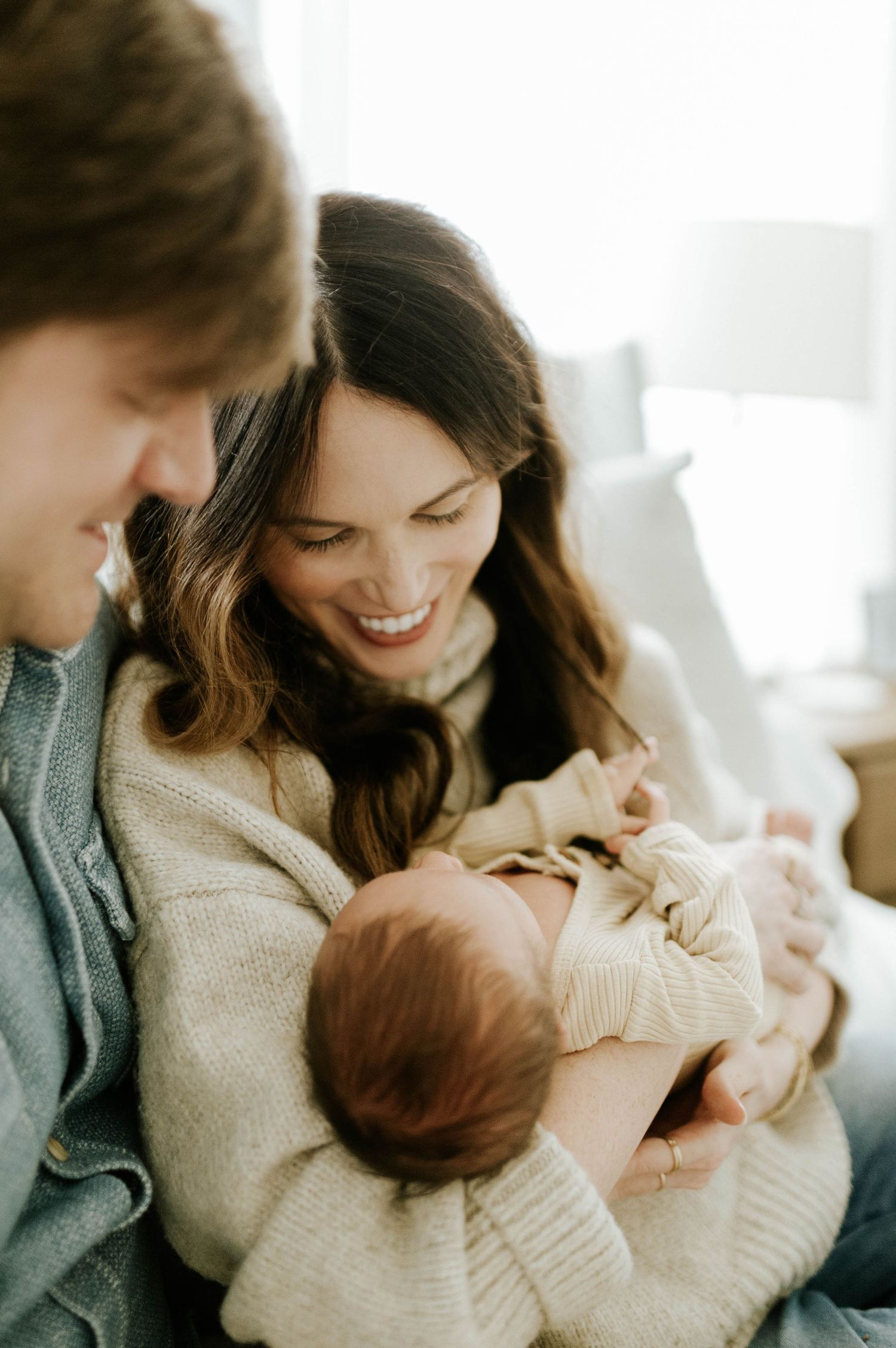 Happy parents smiling and bonding with their newborn baby during an intimate family photo session at home.