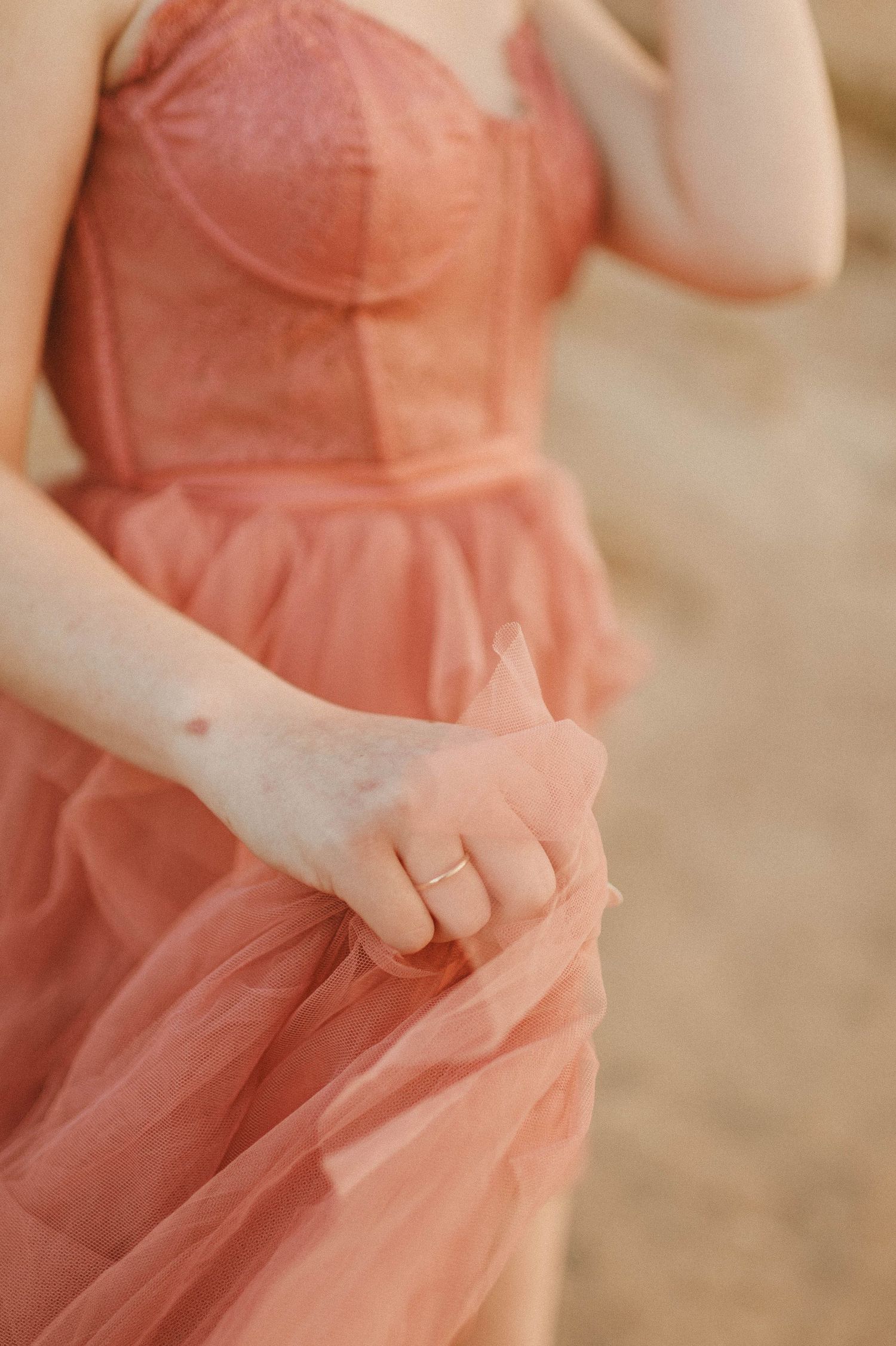 Close-up of woman in dusty rose lace corset tulle gown holding skirt with delicate ring on finger.