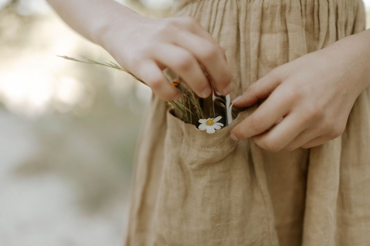 Close-up of hands placing a small daisy flower into pocket of linen dress outdoors.