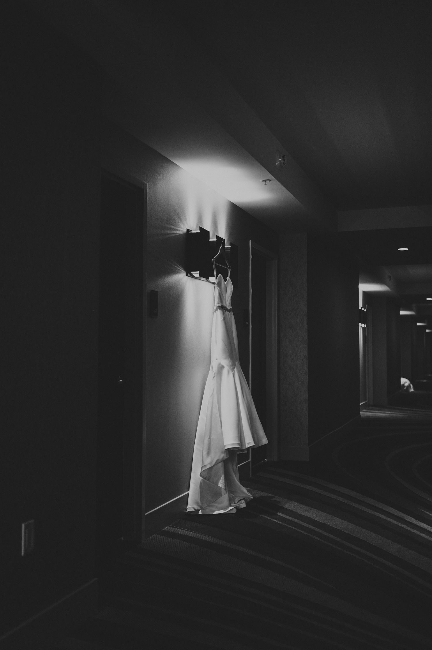 Wedding dress hanging on a wall sconce in a dimly lit hotel hallway.