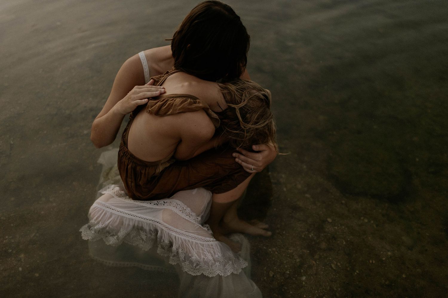 Aerial view of two people in an embrace sitting in shallow water.