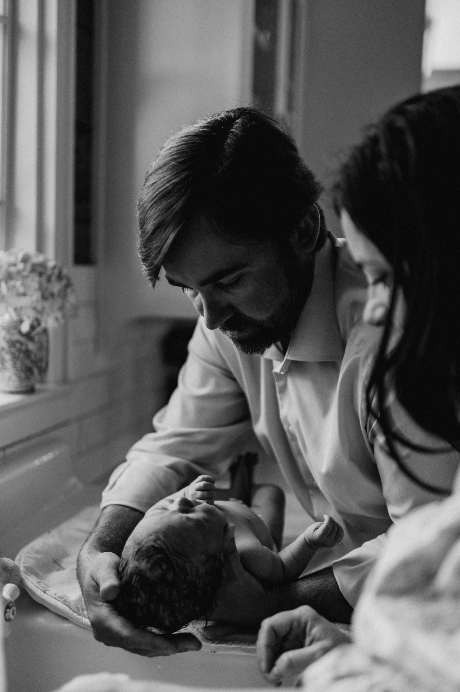 Black and white photo of a bearded father smiling at his newborn baby held in his arms beside the mother.