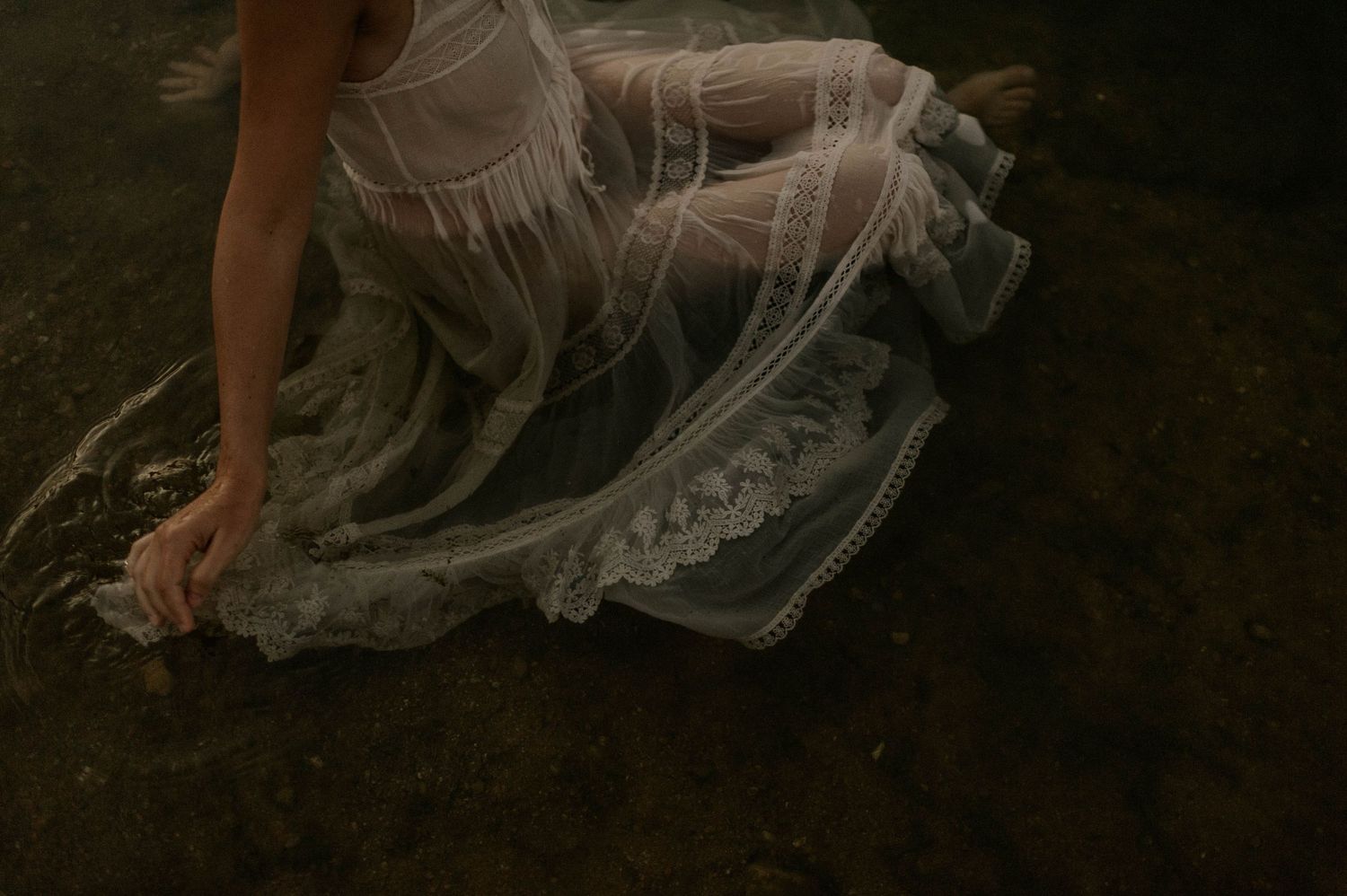 Woman in elegant white lace gown sitting gracefully in shallow water.