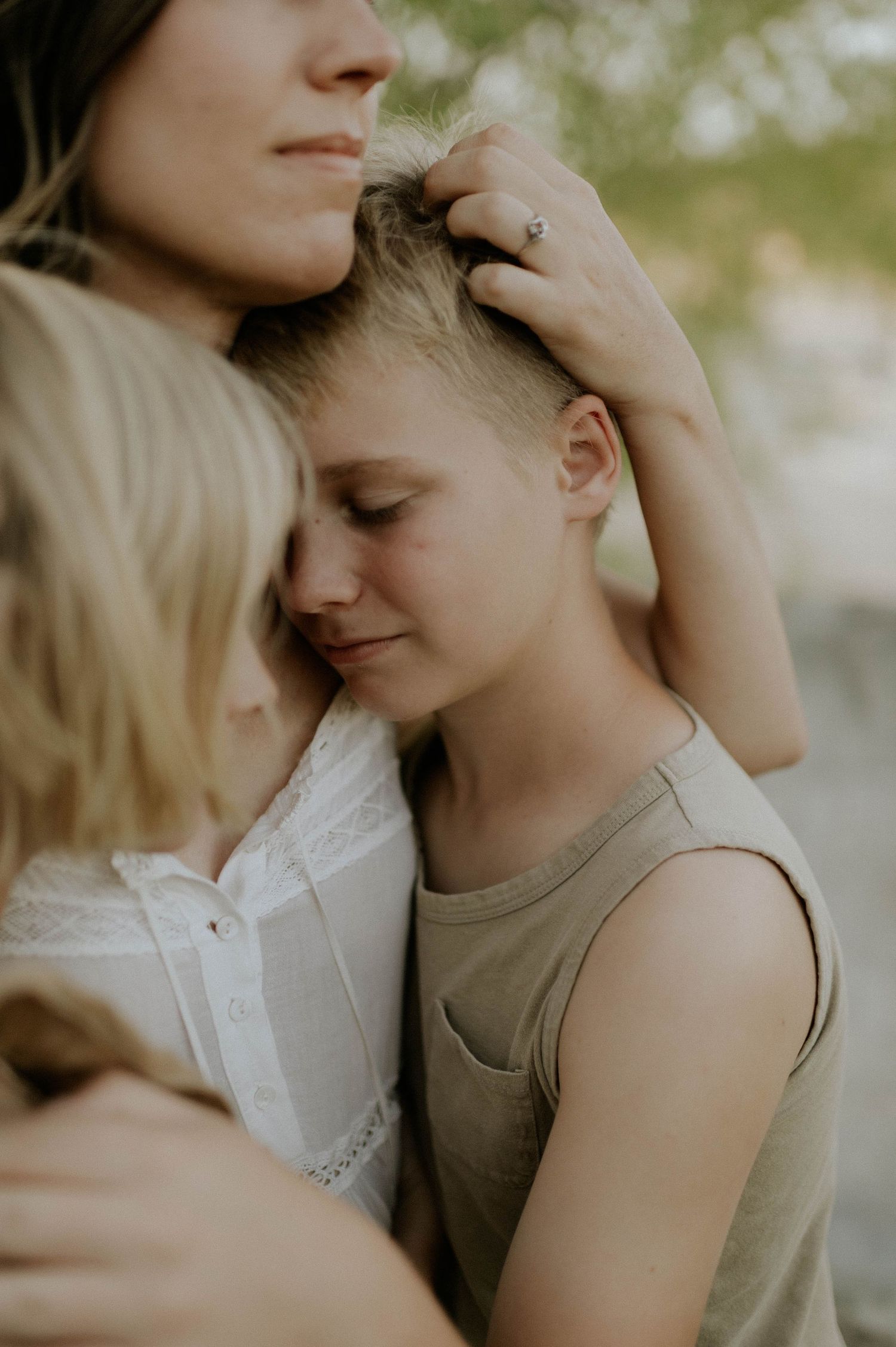 Tender moment of mother stroking childs hair while embracing in warm natural outdoor setting.