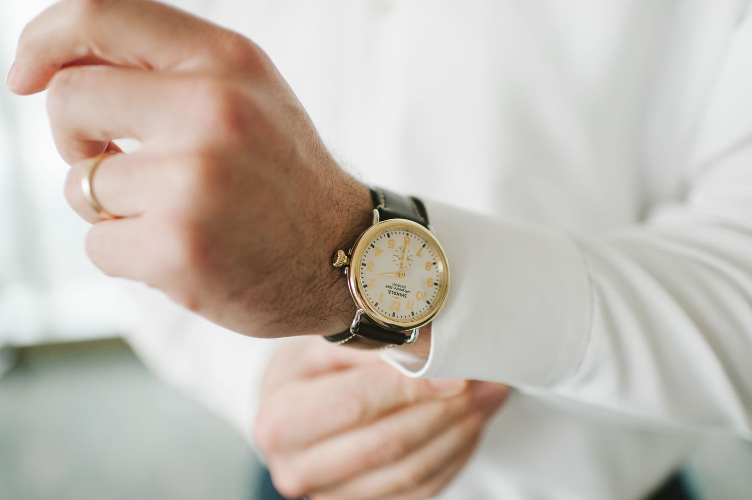 Close-up of a groom adjusting his gold watch while wearing a white dress shirt and gold wedding band.
