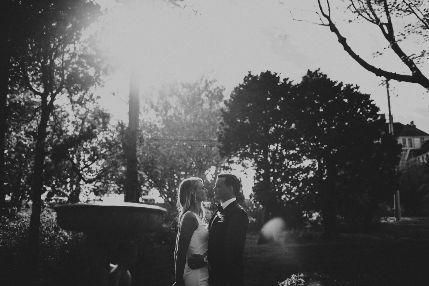 Bride and groom share an intimate moment surrounded by trees with sunlight glowing behind them.