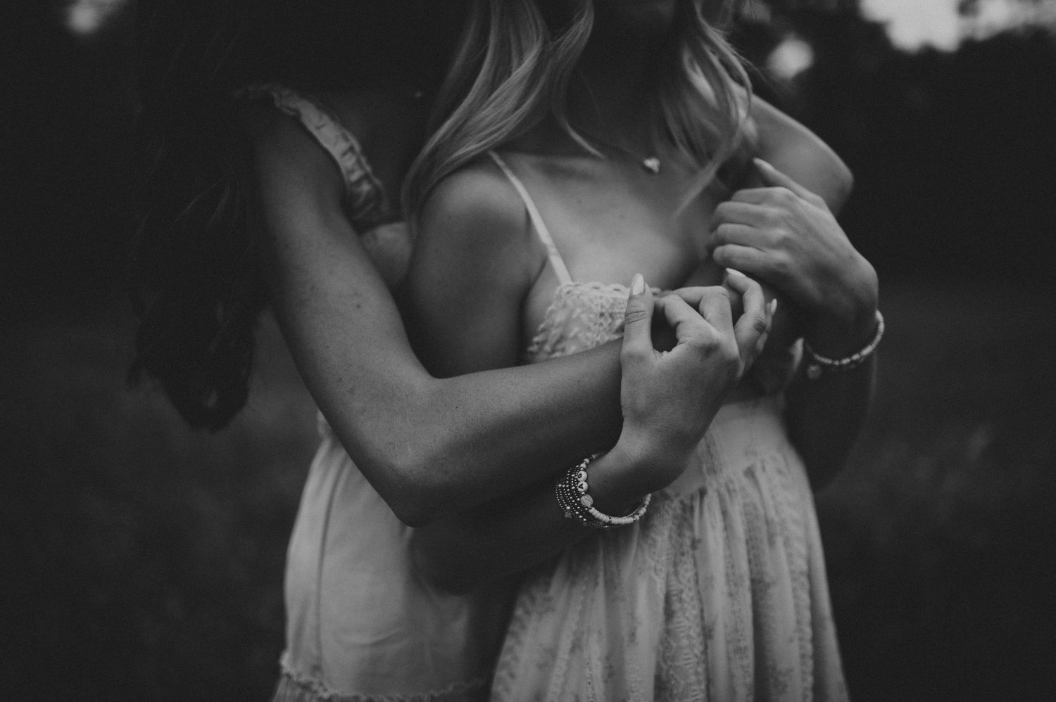 A close-up black and white photo of two women embracing tenderly in an outdoor setting.